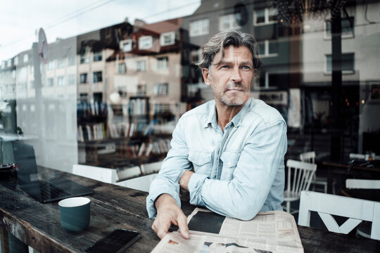 Mature man sitting with newspaper in cafe seen through glass window