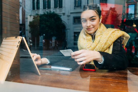 Smiling teenage girl doing online shopping on laptop in cafe