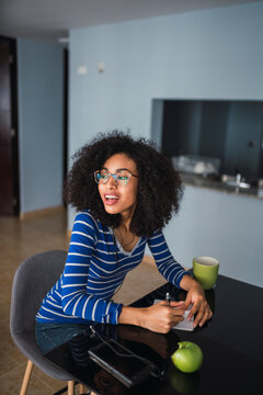Portrait of content young woman sitting at table at home taking notes