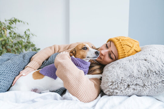 Woman wearing warm clothing cuddling with dog in bed