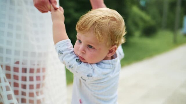 Toddler reaches out to adults in a sunny outdoor setting. The child looks curious and happy while holding hands. Mother smiles warmly at the child, showing affection