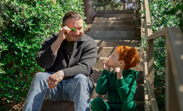 Father and son playfully study a leaf on outdoor park stairs