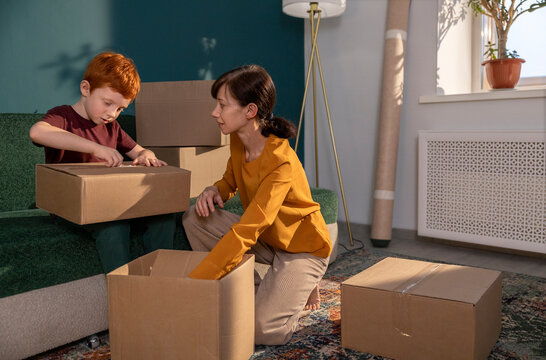 Mother and red-haired boy unpacking boxes in new apartment