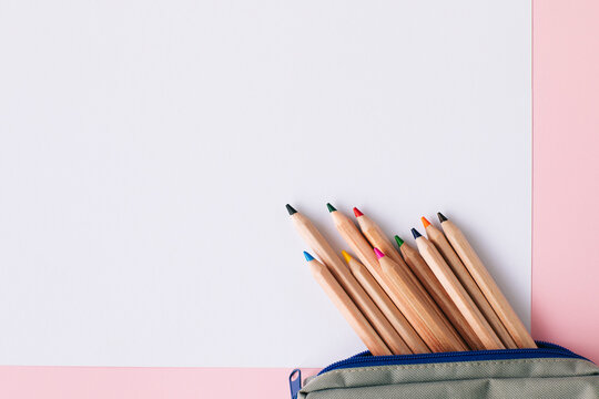 Colored pencils in pouch on blank white paper over pink background