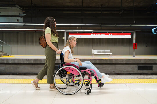 Woman pushing friend in wheelchair on metro station platform