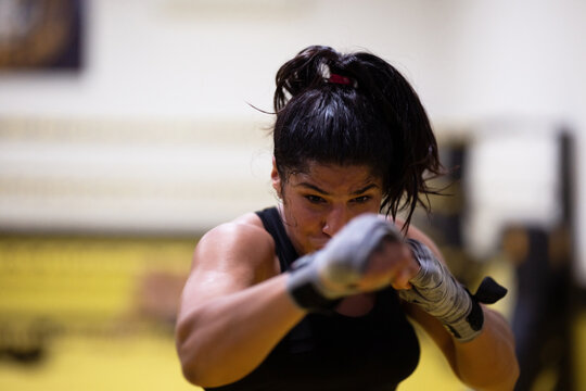 Focused Female Boxer Training With Wrapped Hands Throwing Punch In Gym Workout Session