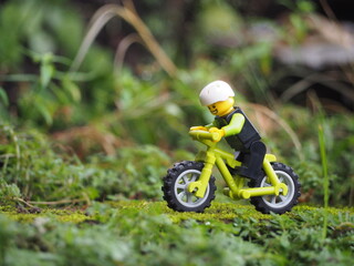 Fototapeta premium Indonesia - May 14, 2022 : Mini toy of action figure at grassland with blurred background. Miniature photography concept. Bicycle at outdoor with green grass conceptual design.