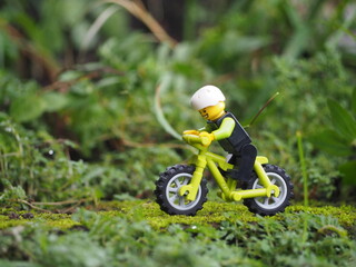 Fototapeta premium Indonesia - May 14, 2022 : Mini toy of action figure at grassland with blurred background. Miniature photography concept. Bicycle at outdoor with green grass conceptual design.