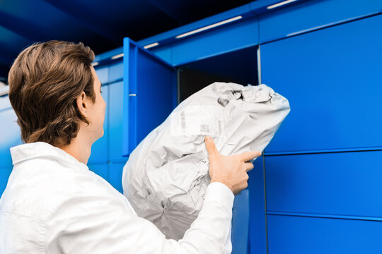 Man picking up a package from a blue parcel locker. Contactless delivery service, online shopping, and e-commerce self-service pickup terminal