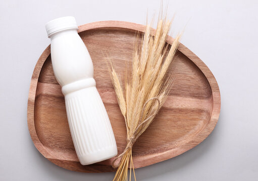 White plastic bottle of cereal yogurt and wheat ears in wooden tray on a gray background. Healthy eating concept.