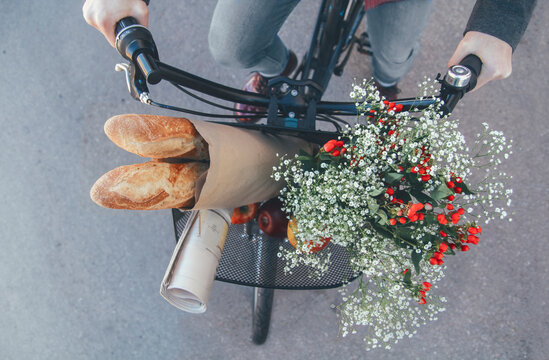 Man with apples, bouquet of flowers, newspaper and baguettes in bicycle basket