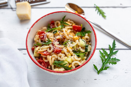 Bowl of noodle salad with corn, cucumber, tomatoes, rocket and grated parmesan