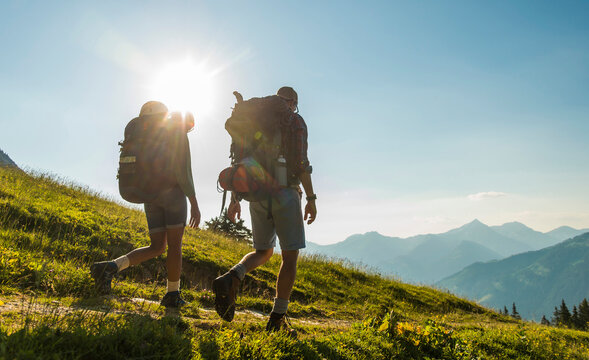 Austria, Tyrol, Tannheimer Tal, young couple hiking on alpine meadow in backlight