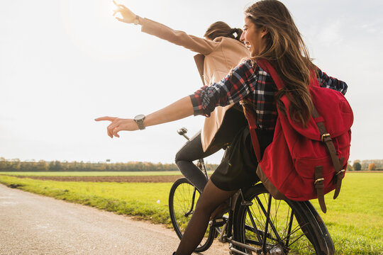 Two exuberant young women sharing a bicycle in rural landscape