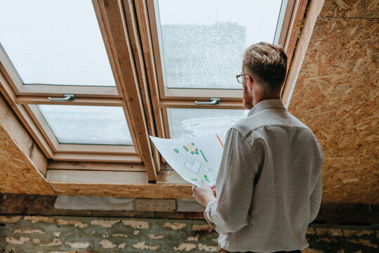 Architect standing with blueprint near window at construction site