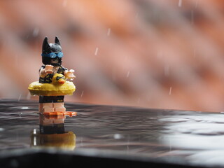Fototapeta premium Indonesia - Novembee 22, 2018 : Mini toy of action figure at table with blurred. Toy photography conceptual design. Enjoying rain with rubber vest concept design. Batman character from DC comics film.