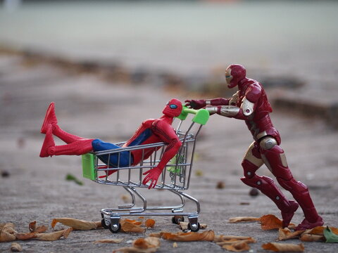 Indonesia - September 12, 2025 : Mini toy of action figure at outdoor with blurred background. Miniature photography concept design. Minifigure of Spiderman and Iron Man character playing trolley.