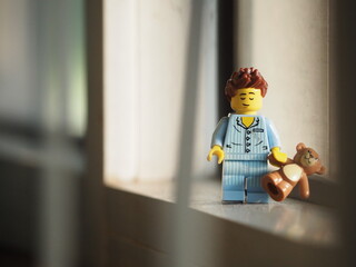 Fototapeta premium Indonesia - September 12, 2025 : Mini toy of action figure at table with blurred background. Miniature photography concept design. Minifigure of people character wearing pajama with teddy bear at home