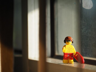 Fototapeta premium Indonesia - September 12, 2025 : Mini toy of action figure at table with blurred background. Miniature photography concept design. Minifigure of young man character with surf board at sunset time.