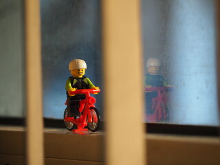 Fototapeta premium Indonesia - September 19, 2019 : Mini toy of action figure at outdoor with blurred background. Miniature photography concept design. Minifigure of young man character riding bicycle at road.