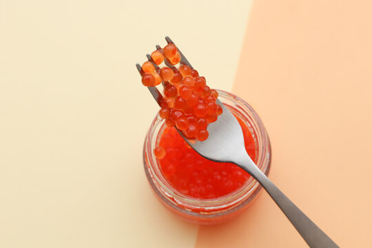 Glass jar of red caviar with fork on a beige background