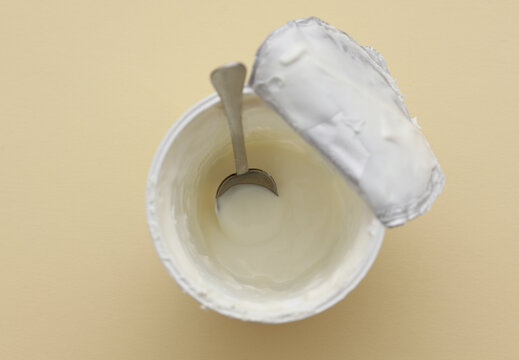 Jar of yogurt with spoon on beige background