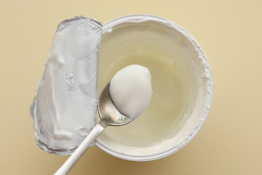 Jar of yogurt with spoon on beige background