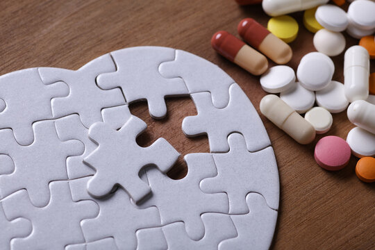 Heart disease treatment. Heart-shaped puzzle and many different pills on a wooden background.