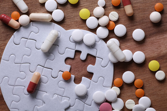 Heart disease treatment. Heart-shaped puzzle and many different pills on a wooden background.