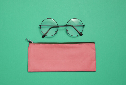 Pink school pencil case with eyeglasses on green background