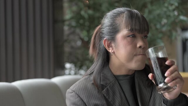 Asian person in a pinstriped blazer sitting on a sofa drinking from glass relaxing
