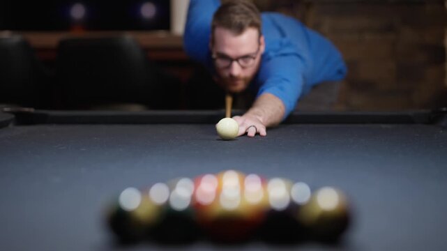 Man lining up a billiards shot on a pool table, with cue ball in focus, blurred racked balls and shallow depth of field in a game room.