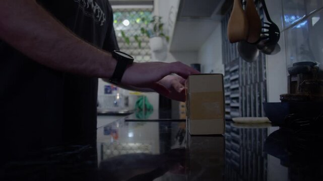 Cinematic 4K shot of a man opening a package with a kitchen knife, inspecting an LED sensor puck light, placing it back in the box and walking away in a modern kitchen.