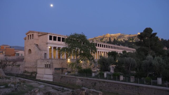Stoa of Attalos with illuminated Acropolis on the hill at twilight overlooking Athens' ancient agora.
