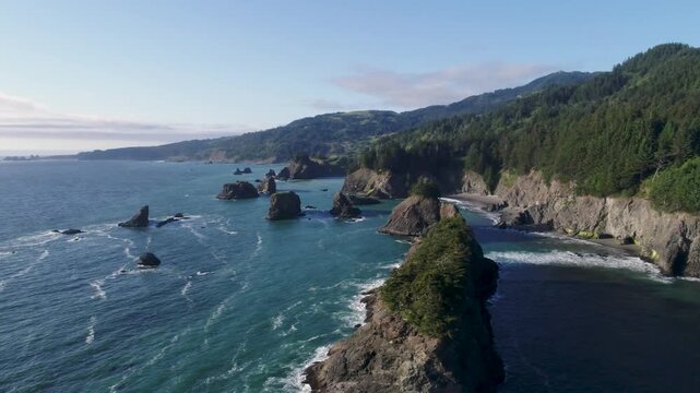An unworldly drone shot, descending below the tree line of a massive sea-stack, big enough to home a small forest, near 'Arch Rock', and 'Secret Beach', along Oregon's southern coast.