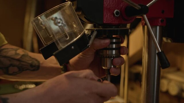 Tattooed male carpenter with tattoos installing drill bit into drill press chuck in workshop, close up. Footage is perfect for vocational training videos, manufacturing promos, and DIY tutorials