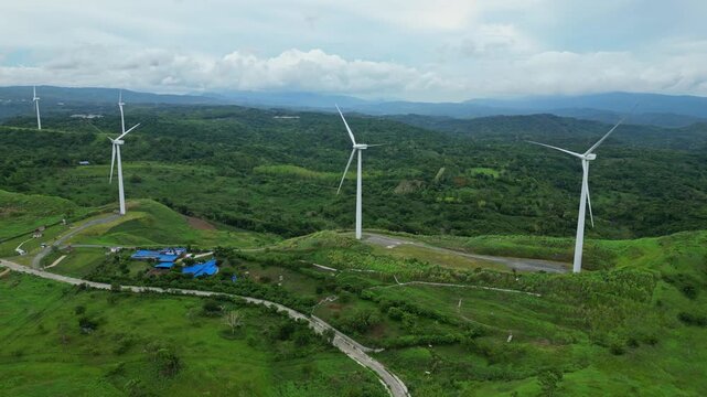 Aerial panorama of Pililla Wind Farm, Rizal Province with giant wind turbines, Sierra Madre mountains, and Laguna de Bay visible in the background.