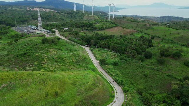 High altitude aerial view of wind turbines in Pililla, Rizal with rolling mountains, vegetation, and rural communities in the background.
