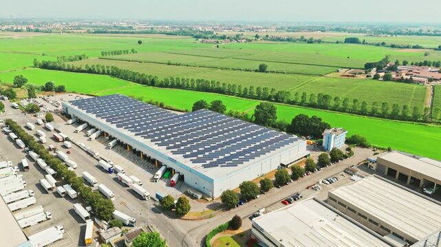 Aerial footage of a modern logistics center with solar panels on the roof. Numerous trucks are loading and unloading goods at the docks