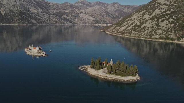 Cinematic drone shot of Saint George Island and Our Lady of the Rocks islet surrounded by calm waters in the scenic Bay of Kotor, Montenegro.