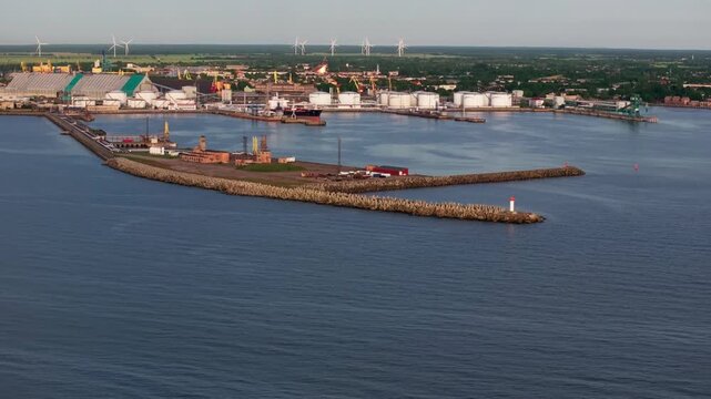 Drone aerial footage overlooking the oil terminal and industrial harbor in Ventspils, Latvia. The video features a tanker at the petroleum terminal, extensive fuel storage facilities, a breakwater wit