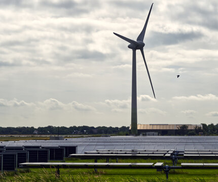 Wind turbine standing tall over a field of solar panels, collectively producing sustainable green energy