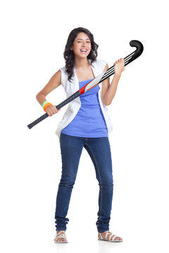 Full length portrait of young woman in casuals holding hockey stick over white background 