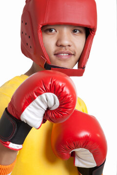 Portrait of young boy wearing boxing gloves and head protector over white background 