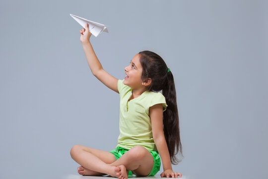 Little girl playing with paper airplane isolated over blue background 