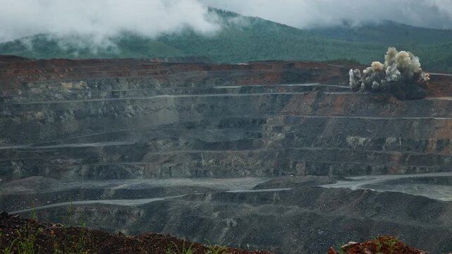 Slow motion explosive blast in open pit mine quarry with smoke and dust on mountainside.
