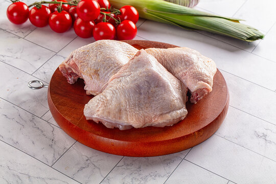 Raw chicken thighs on wooden cutting board with cherry tomatoes and leek