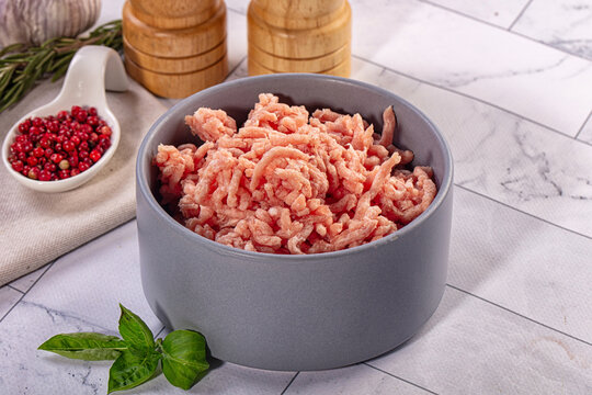 Raw ground meat in gray bowl with fresh basil and red peppercorns on marble surface