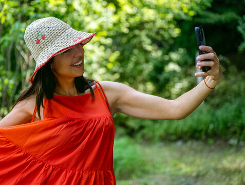 Beautiful woman with straw hat and red dress making selfie with the phone in the summer