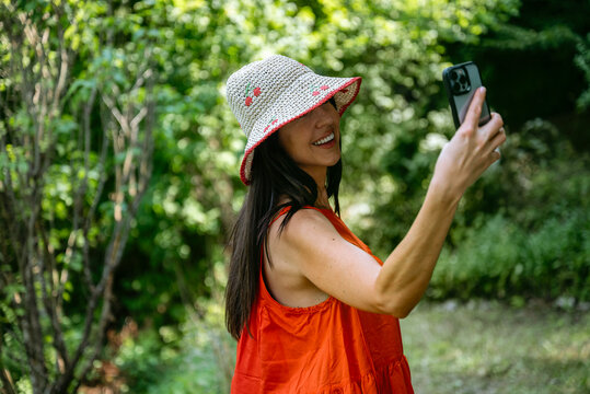 Beautiful woman with straw hat and red dress making selfie with the phone in a green garden 